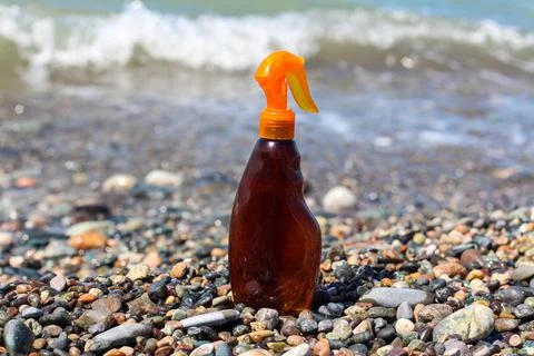 Sun tanning spray bottle in front of the waves at the sea coast Stock Photos