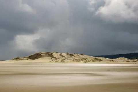 Sun through patches dark cloud create pattern on sand in foreground to dune.. Stock Photos