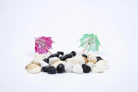 Sun umbrella with sunlight shadow on different sea shells and white stones. Stock Photos