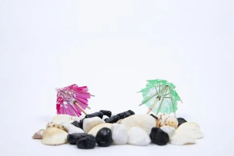 Sun umbrella with sunlight shadow on different sea shells and white stones. Stock Photos