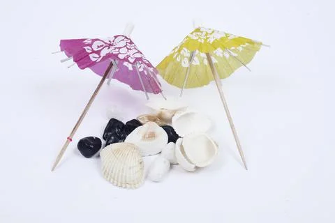 Sun umbrella with sunlight shadow on different sea shells and white stones. Stock Photos
