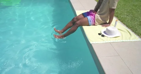 Sun urging African American man sitting at backyard pool testing splashing Stock Footage 344341128
