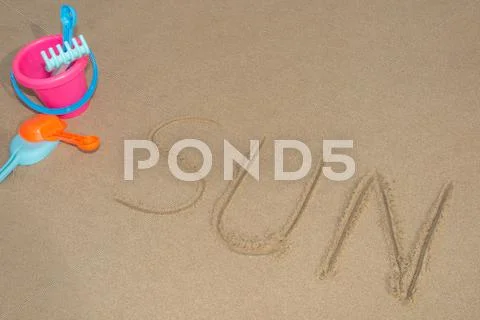 Sun written in Sand on a Beach with beach toys Stock Photos