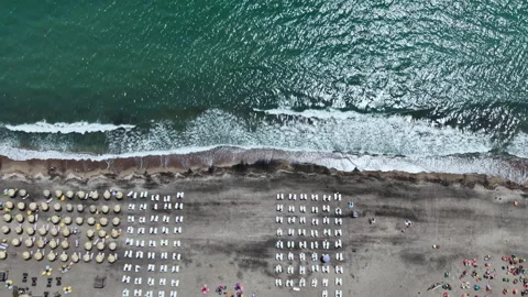 Sunbathers relax on beach chairs by the ocean as waves crash on the shore during Stock Footage 337877806