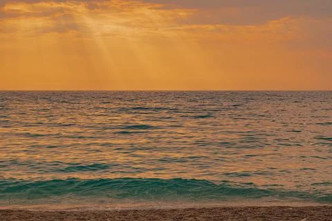 Sunbeams breaking through clouds over calm sea waves at sandy beach shoreli.. Stock Photos