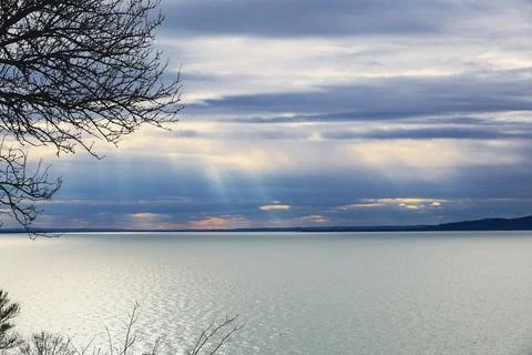 Sunbeams breaking through layered clouds and illuminating wide lake Stock Photos