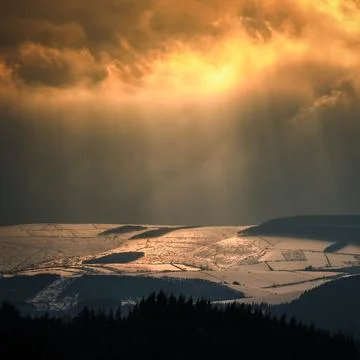Sunbeams filter through the clouds and tinge with gold the snowy hills Fotos Stock