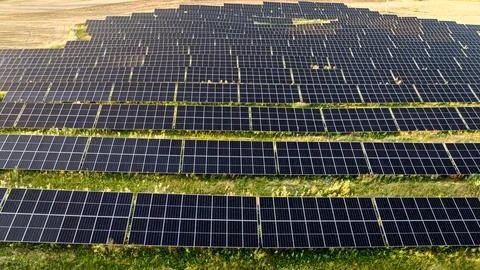 Sunbeams over a blue solar array on green field, aerial. Stock Photos