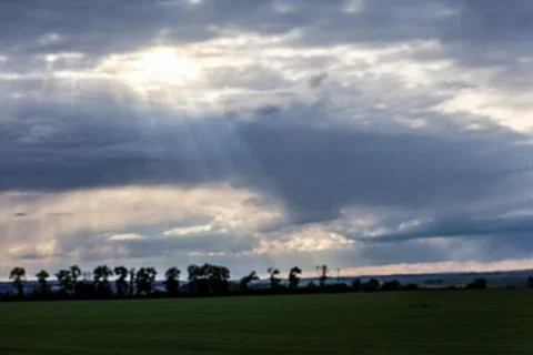 Sunbeams pierce through dramatic storm clouds over a green field Foto stock