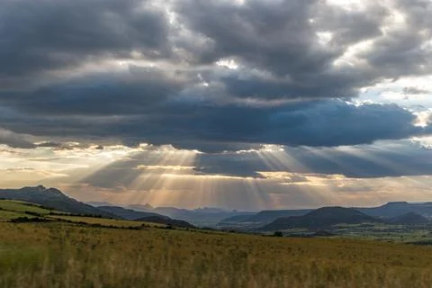 Sunbeams Piercing Through Clouds Over the Lush Green Valleys Stock Photos