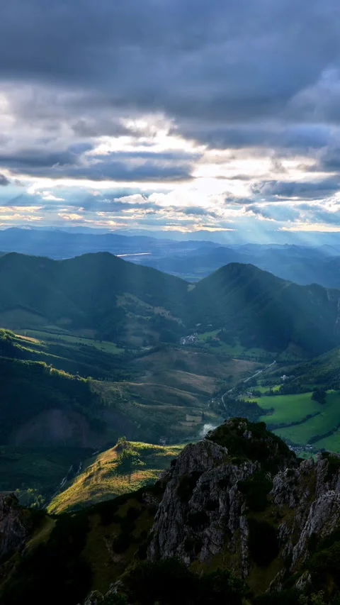 Sunbeams shine through moving clouds at sunset. Rays illuminate the hilly Video stock 284759952