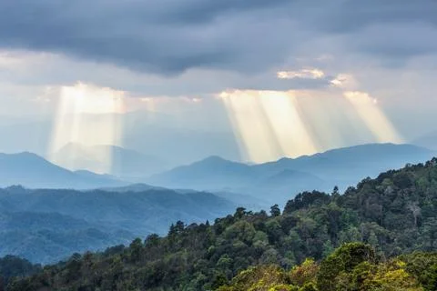 Sunbeams shining through cloudy sky to blue mountains Stock Photos