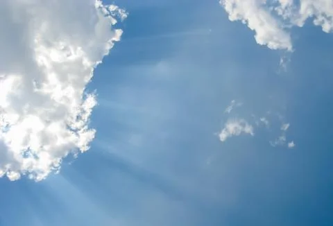 Sunbeams through fluffy white clouds in a blue sky Stock Photos