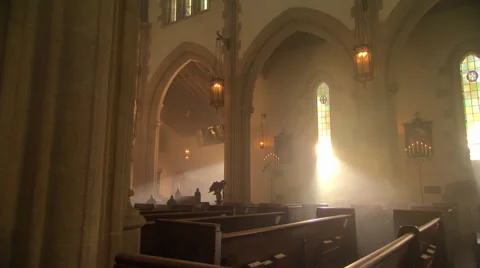 Sunbeams through stained glass windows in Catholic church, nun walking up aisle Stock Footage