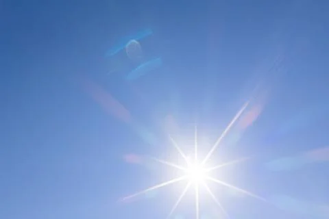 Sunburst against a cloudless blue sky with colorful optical lens flare 스톡 사진