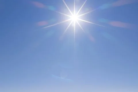 Sunburst against a cloudless blue sky with colorful optical lens flare Stock Photos
