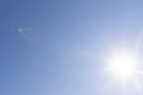 Sunburst against a cloudless blue sky with colorful optical lens flare Stock Photos