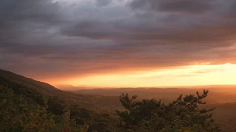 Sunburst light cutting through storm clouds, mountain ridge and valley below Stock Footage 323575332