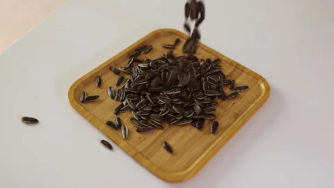Sunflower seeds being poured onto a square wooden plate. Stock Footage 344646514