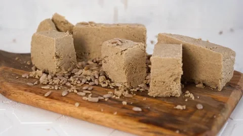 Sunflower seeds fall to the dessert halva or sesame on a wooden cutting board. Video stock 170457935