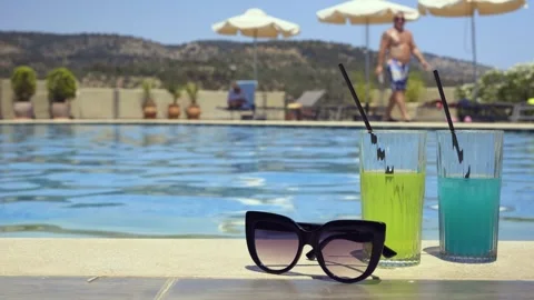 Sunglasses and colorful drinks by a pool on a sunny day, summer relaxation Stock Footage 328669364