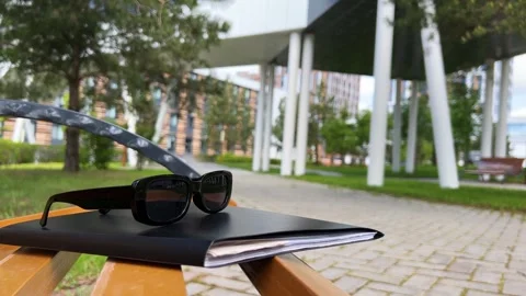 Sunglasses are lying on documents in a folder on a bench on a sunny summer day Stock Footage 252414389
