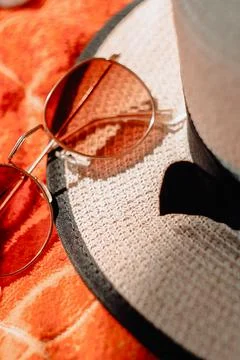 Sunglasses on an orange towel next to a wicker hat Stock Photos