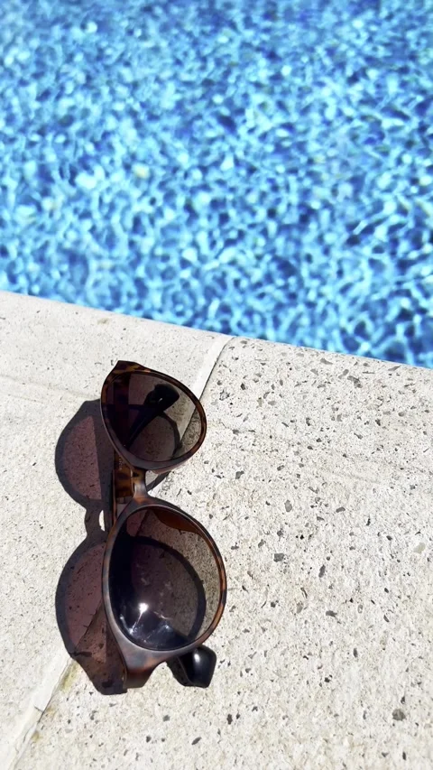 Sunglasses on Poolside Edge with Sparkling Water in Background Video stock 344536695