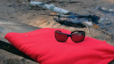 Sunglasses on red plaid on bonfire background in forest camping. Video stock 135993867
