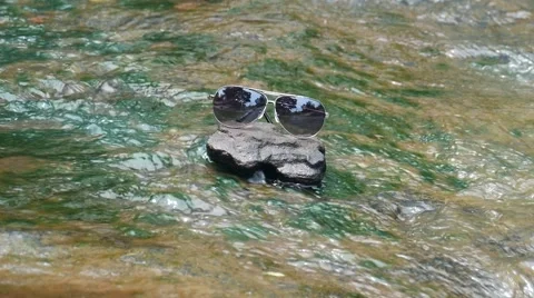 Sunglasses on rock with waterfall background, Stock-Footage 66380752
