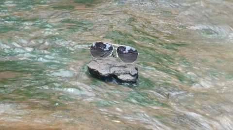 Sunglasses on rock with waterfall background, 스톡 동영상 68344194