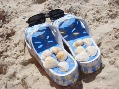 Sunglasses on slippers with shellfish at a beach Stock Photos