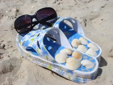 Sunglasses on slippers with shellfish at a beach Stockfoto's