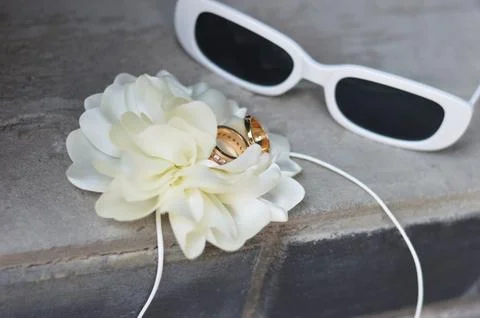 Sunglasses, a white flower and the bride and groom's rings lie on a gray conc Stock Photos