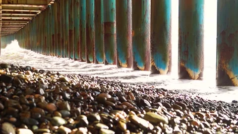 Sunlight and a huge wave beat through the rusty supports of the bridge Stock Footage 171603964