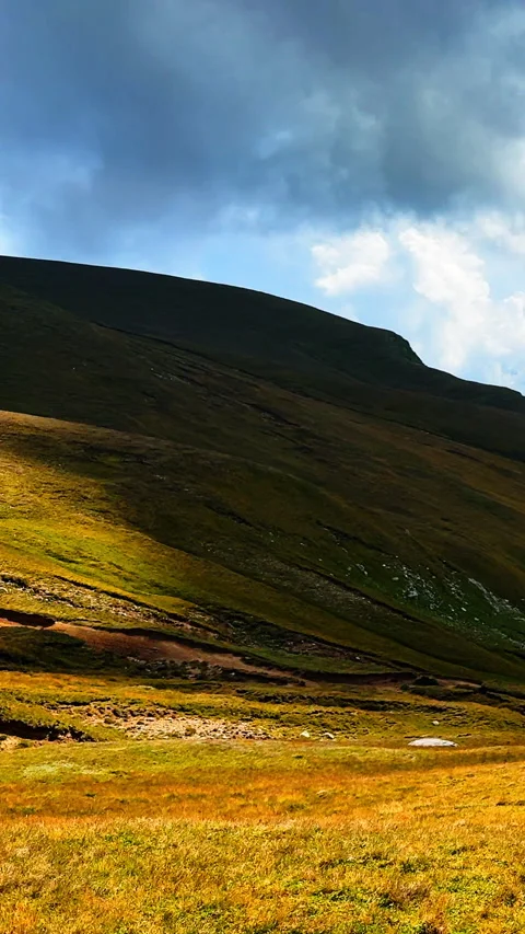 Sunlight and shadow on grassy mountain slope under cloudy sky Stock Footage 329915140