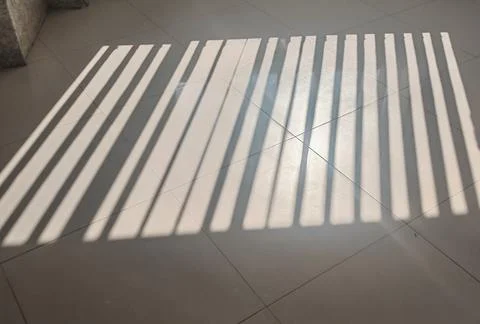 Sunlight and shadow patterns from window blinds on ceramic tile floor Stock Photos
