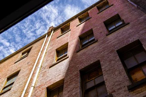 Sunlight and shadows interplay on the textured, aged brick wall of an urban.. Stock Photos