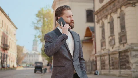 At sunlight attractive bearded man use call on phone walking on city street look Stock Footage 140479756