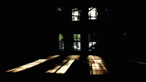 Sunlight beams piercing through tall arched windows into darkened interior 库存影片 344411652