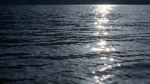 Sunlight  blinking on water surface. Boat and another mountain shore in far Stock Footage 124027480