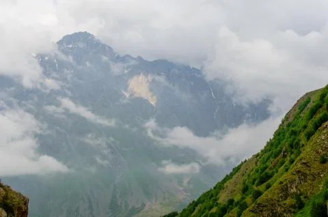 Sunlight break through smoky clouds hanging over a large great green mountain Stock Photos