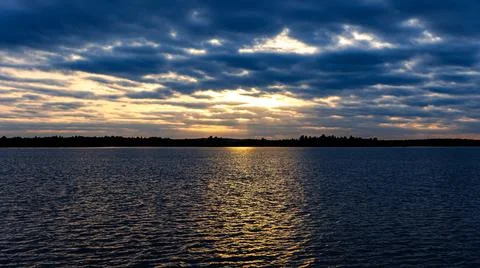 The sunlight is breaking through the clouds above the water surface Stock Photos