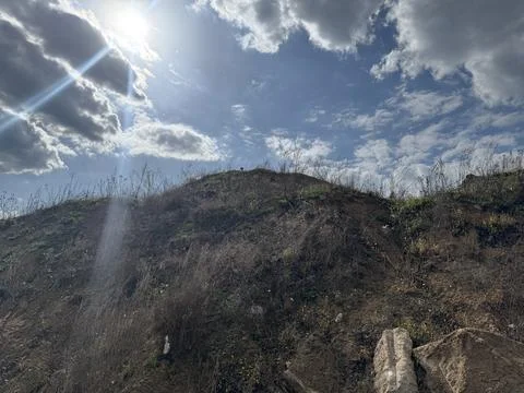 Sunlight breaking through clouds over a rugged grassy hillside Stock Photos