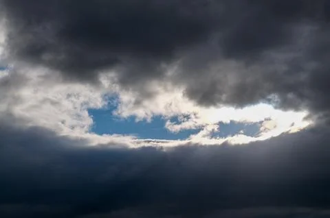 Sunlight breaking through dark storm clouds with a patch of blue sky Stock Photos