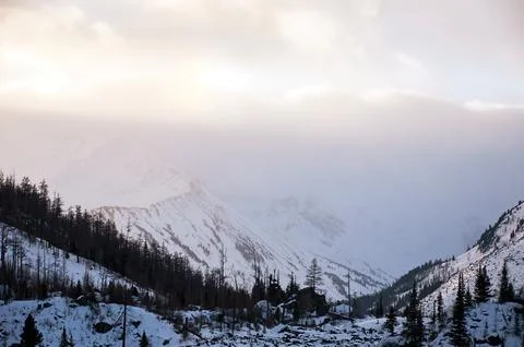 Sunlight breaks through clouds above snowcovered mountains. Stock Photos