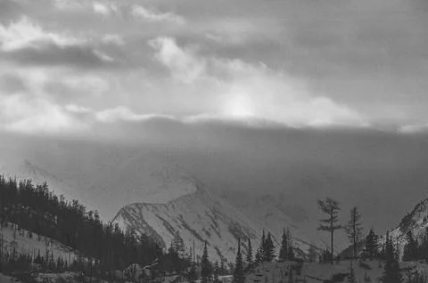 Sunlight breaks through clouds above snowcovered mountains. Stock-Fotos