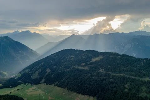 Sunlight breaks through clouds over tranquil mountains at dusk, revealing lush Stock Photos