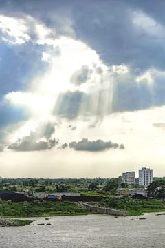 Sunlight breaks through clouds over the river and town on a cloudy day. Stock Photos