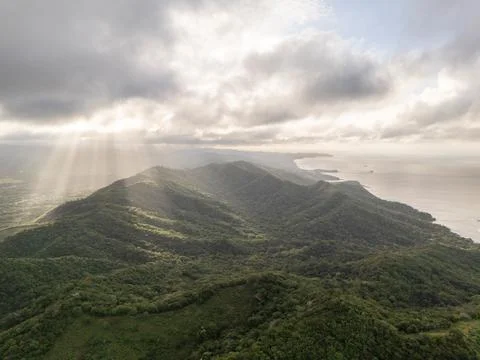 Sunlight breaks through clouds over lush green hills by the coast Stock Photos